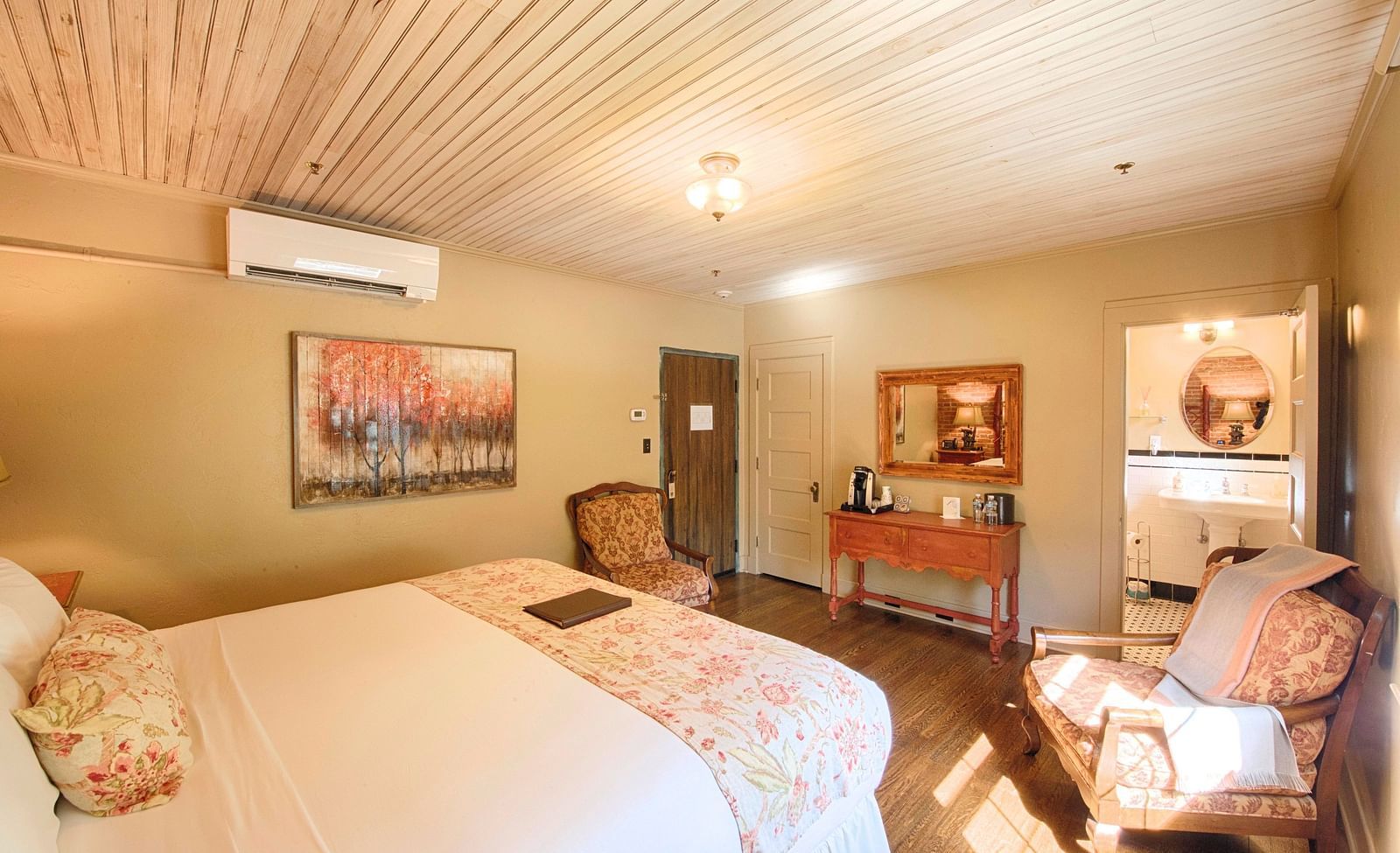 corner view image of a bedroom with two armchairs facing towards each other in front of the bed along with a wall mounted air-conditioner - Historic Tapoco Lodge