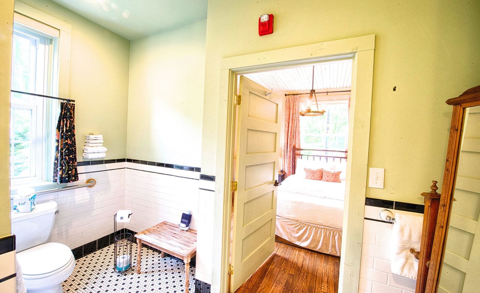 a brightly lit bathroom with a commode and rack in the corner featuring a door opening to the bedroom - Historic Tapoco Lodge