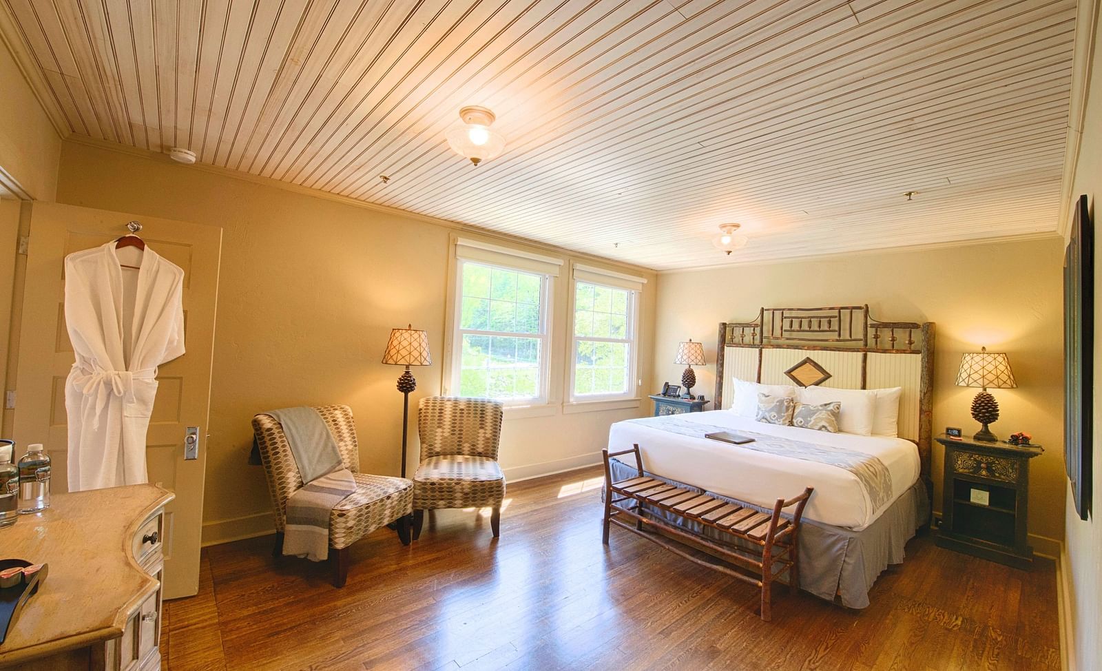 full view image of a bedroom with a plush double bed with a beautiful headboard and a bathrobe hanging on the bathroom door - Historic Tapoco Lodge