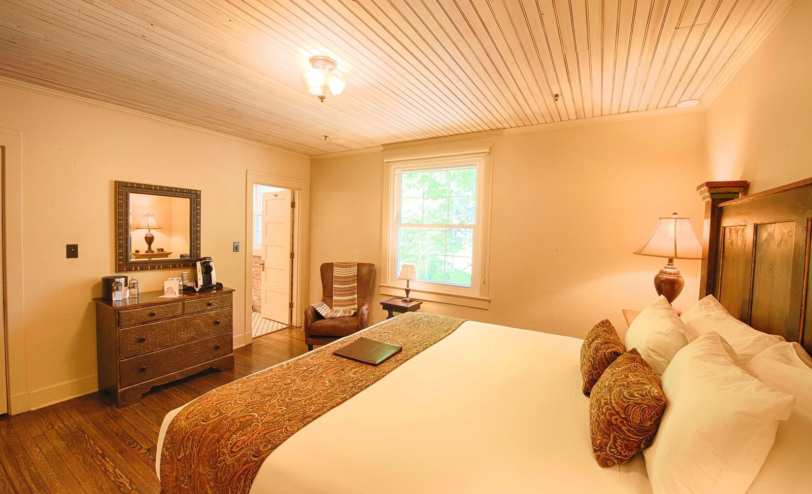 corner view image of a bedroom featuring a plush soft double bed with a small window in the far end of the room - Historic Tapoco Lodge