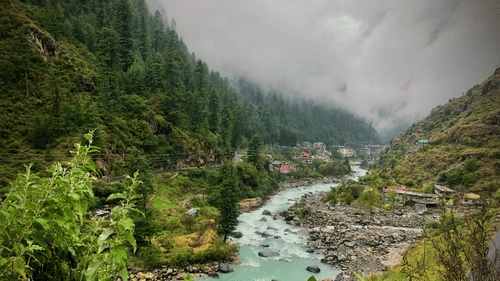 A river winds through a lush green valley in Kasauli.