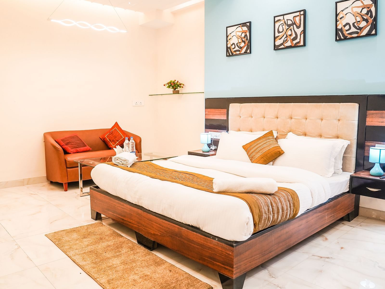 A neatly arranged room features a double bed with patterned bedding, a chair, and framed pictures on the wall - Asian Suites Cyber Park, Gurgaon