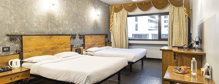 A neatly arranged room with 2 king size bed, textured grey wall, bedside tables, a desk, and warm lighting at Infiniti Hotel, Indore.