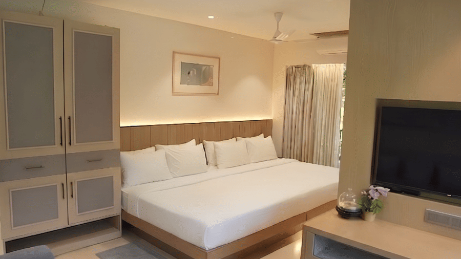 A spacious room features a king size bed, a television console, a wardrobe, and a sofa seating area under a ceiling fan at Bougainvillea, Alibaug.