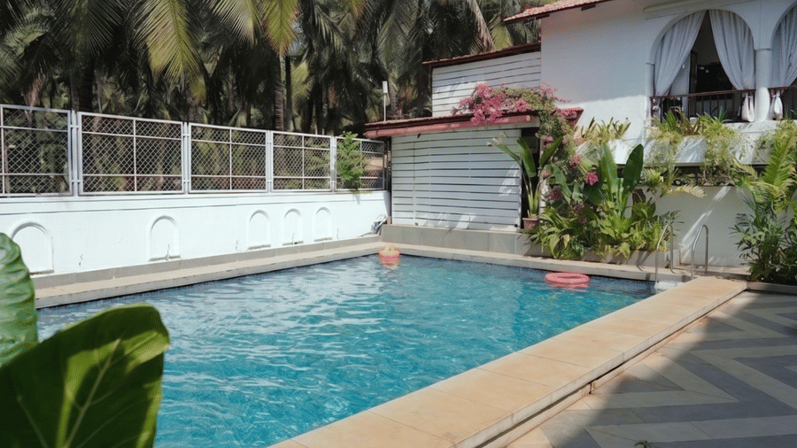Sun loungers with striped towels rest by a swimming pool, flanked by a small table, tropical plants at Bougainvillea, Alibaug.