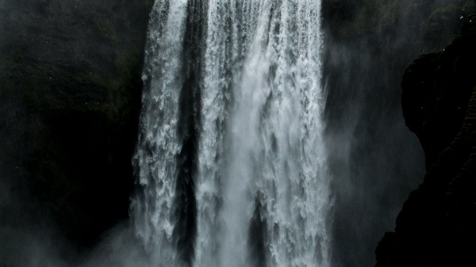 A waterfall cascading from a mountain with dark clouds covering the sky