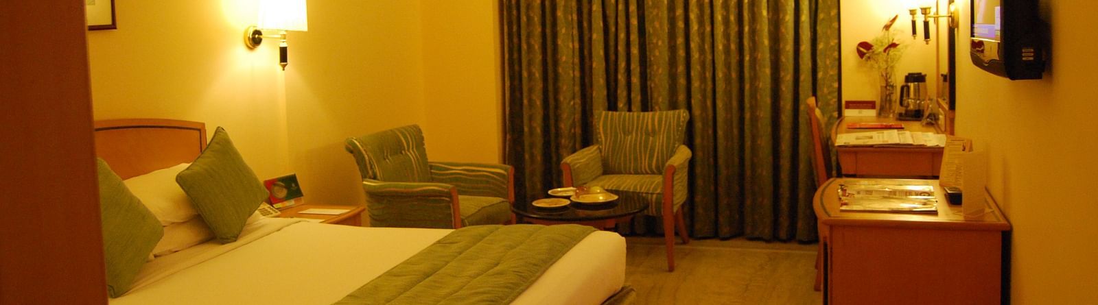 A photo showing a room with bright lights where a large bed, two chairs, and a flat screen TV are visible.