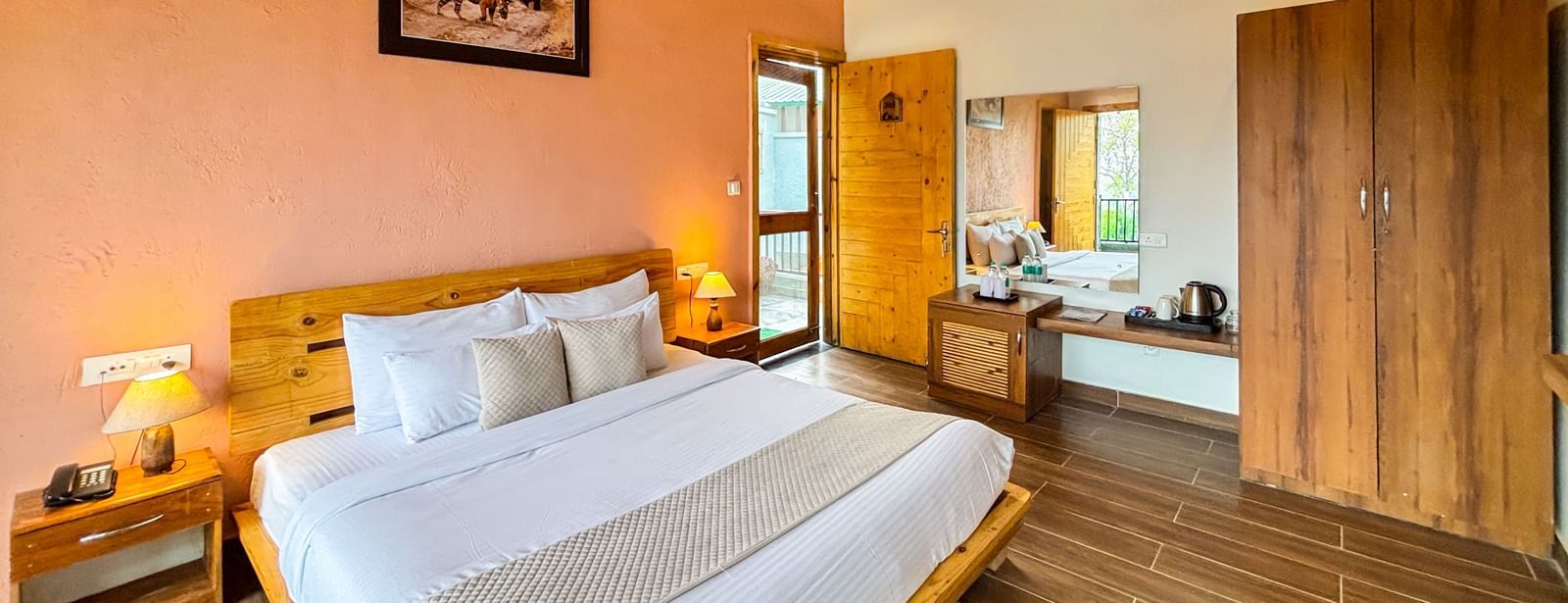 A cosy bedroom with a sloped wooden ceiling, a large bed, and warm-toned walls at Corbett Nirvana Resort..