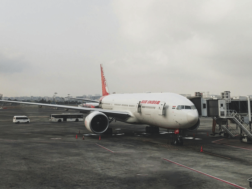 A white and orange aeroplane parked on a grey airport runway under an overcast sky, viewed through a window.
