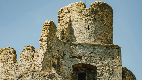 A tall, weathered stone tower or section of a historic castle wall flying a red and white flag.