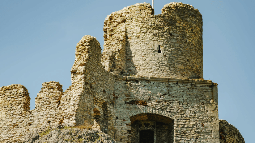 A tall, weathered stone tower or section of a historic castle wall flying a red and white flag.