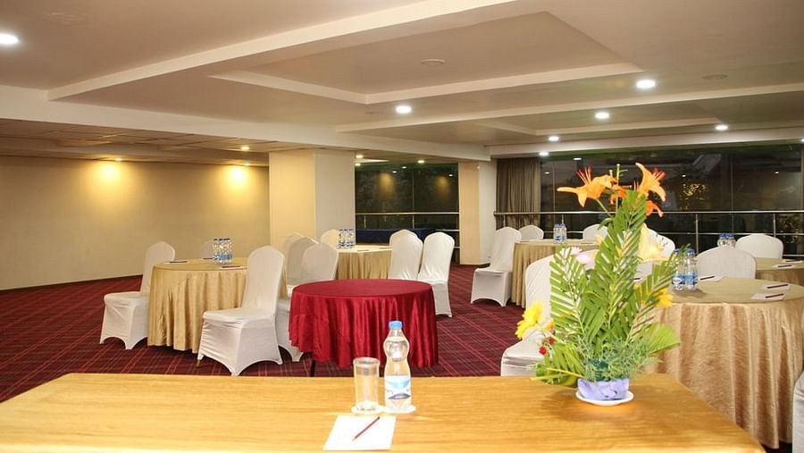 Empty chairs facing the stage alongside tables covered in decorative clothes, beside a rectangular table with a flower vase on top - Monarch Hotels