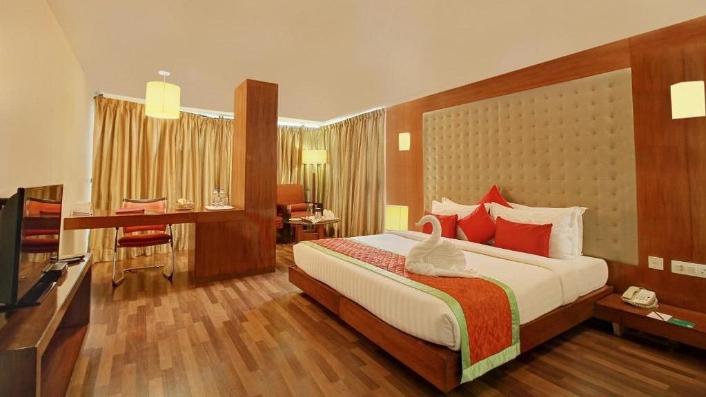 Spacious hotel room with a king size bed, decorative pillows, a work desk, seating area, and warm lighting - Monarch Hotels