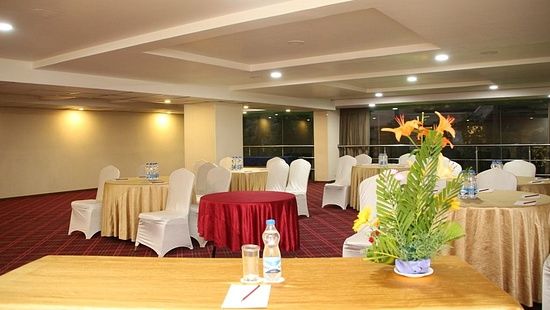 Empty chairs facing the stage alongside tables covered in decorative clothes, beside a rectangular table with a flower vase on top - Monarch Hotels