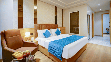 A bedroom at Hotel 91 HUDA Premier, Gurugram with a king size bed, pillows, sofa chair, table, and wall panels.