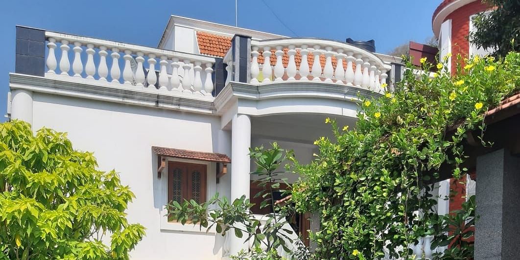 Facade of  Villa Serenity Le Sejour Pondicherry with a swimming pool in front and plants on the side.