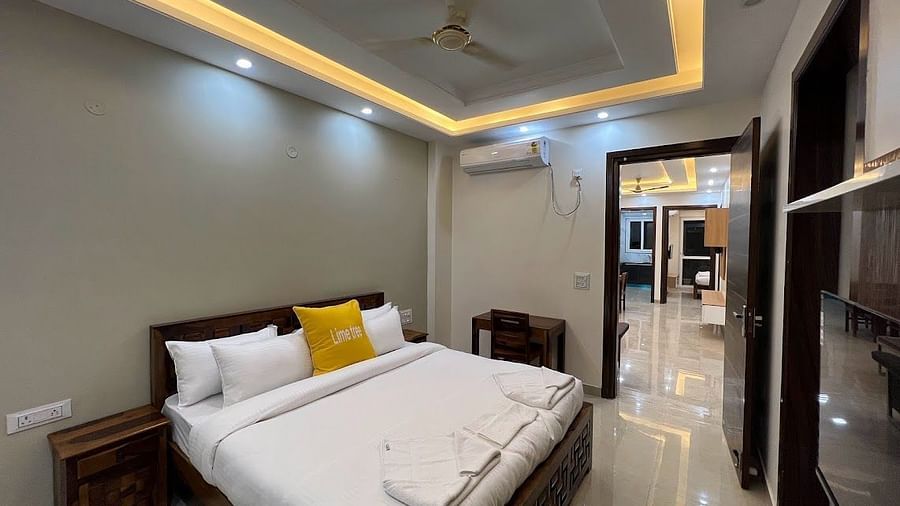 An image of a bedroom featuring a double size bed, a bedside table, a flat TV screen, a work desk and chair, and cabinets around the room - Lime Tree 2BHK Serviced Apartment Golf Course Road