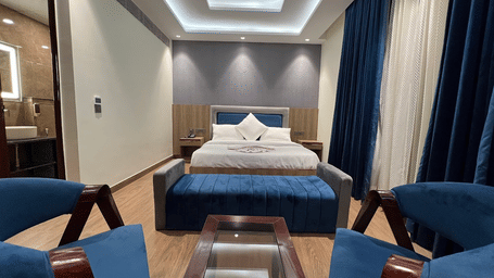 Suite of Lime Tree Hotels & Service Apartment Private Limited featuring teal armchairs, a bed, and cove lighting.