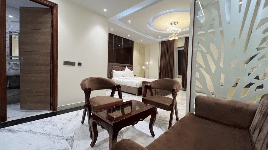 Suite of Lime Tree Hotels & Service Apartment Private Limited featuring brown armchairs, a decorative partition, and white bedding.
