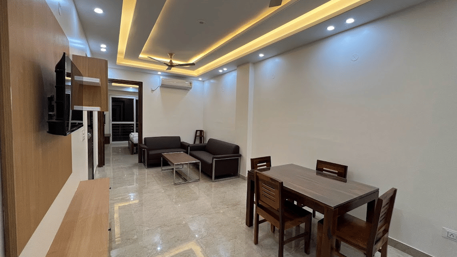 Living and dining area of Lime Tree Hotels & Service Apartment Private Limited featuring a dark sofa, a dining table, and cove lighting.