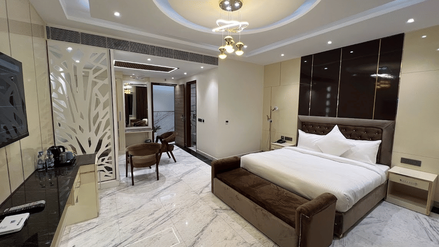 Suite of Lime Tree Hotels & Service Apartment Private Limited featuring dark wood furnishings, a wall mounted television, and white bedding.