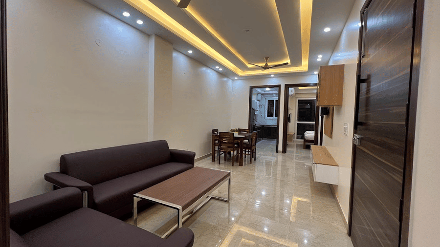Living room of Lime Tree Hotels & Service Apartment Private Limited featuring a purple sofa, a coffee table, and a view towards the corridor.