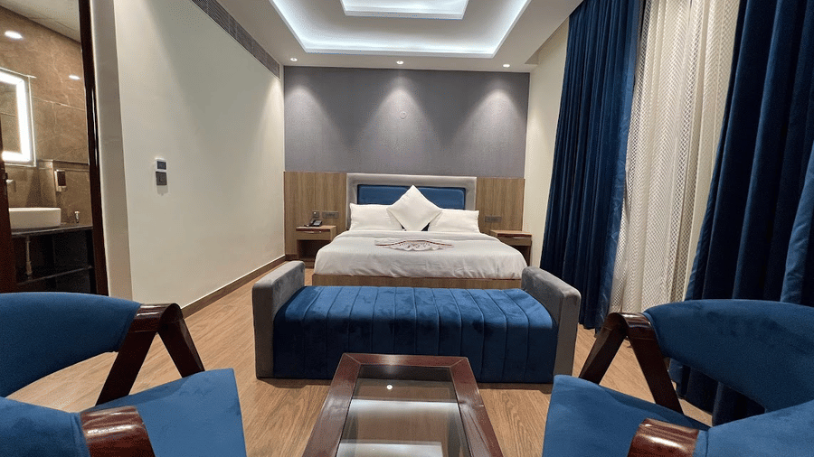 Suite of Lime Tree Hotels & Service Apartment Private Limited featuring teal armchairs, a bed, and cove lighting.