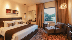 Guest room at Pride Premier Pune featuring a king size bed, seating area and large window with city views.