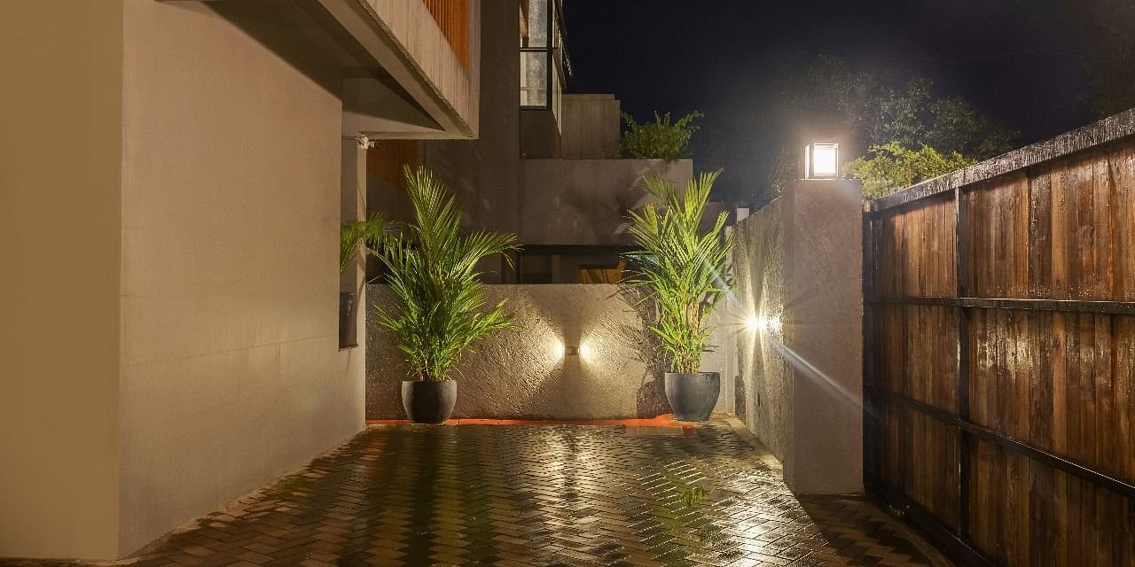 Night view of the entrance pathway at Lindsay Manor with tiled flooring, potted plants, and wooden fencing.