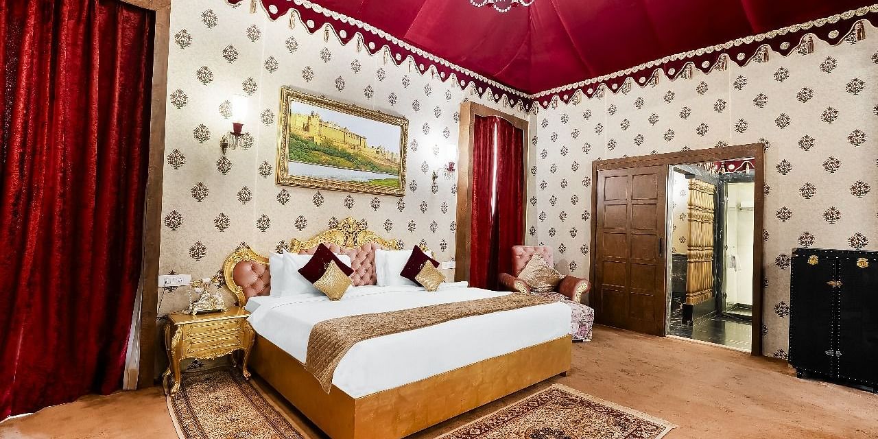 Side view of a  lavishly decorated tent suite at the Rajasthali Resort & Spa in Jaipur features a four-poster bed, ornate furnishings, and a red draped ceiling.