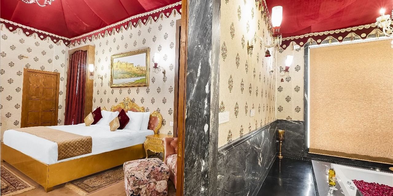  A bedroom interior at the Rajasthali Resort & Spa in Jaipur, featuring a bed with white linens and a brown accent runner, flanked by bedside tables and lamps. T