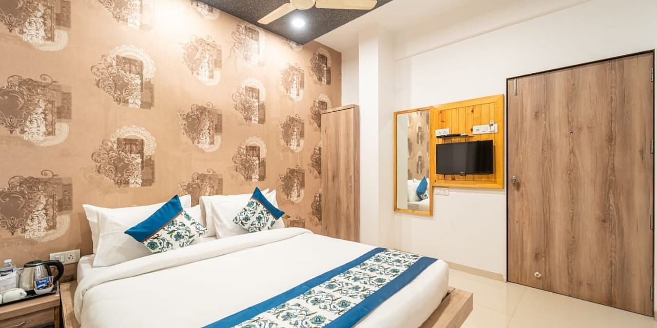 A room featuring a bed with blue and white linens, a patterned wallpaper, a ceiling fan, a television, and a wooden closet. 