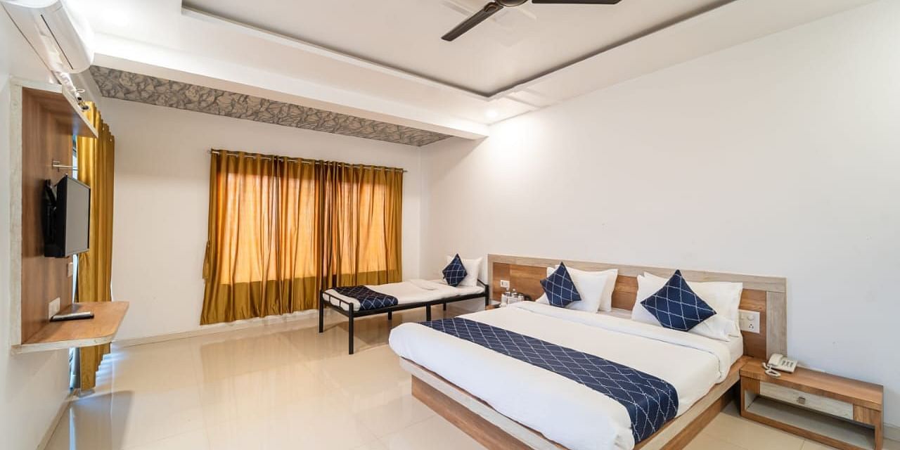 Penthouse Suite with Balcony featuring a king size bed with white linens and a gray accent runner, two blue decorative pillows, bedside tables, a mattress, and a ceiling fan.