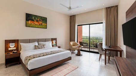Classic Room with Sitout and Pool View at Osian Valley Resort & Spa, Kumbhalgarh, featuring a king size bed, armchair, work desk, wall mounted television, and large window opening towards the sitout and pool view.