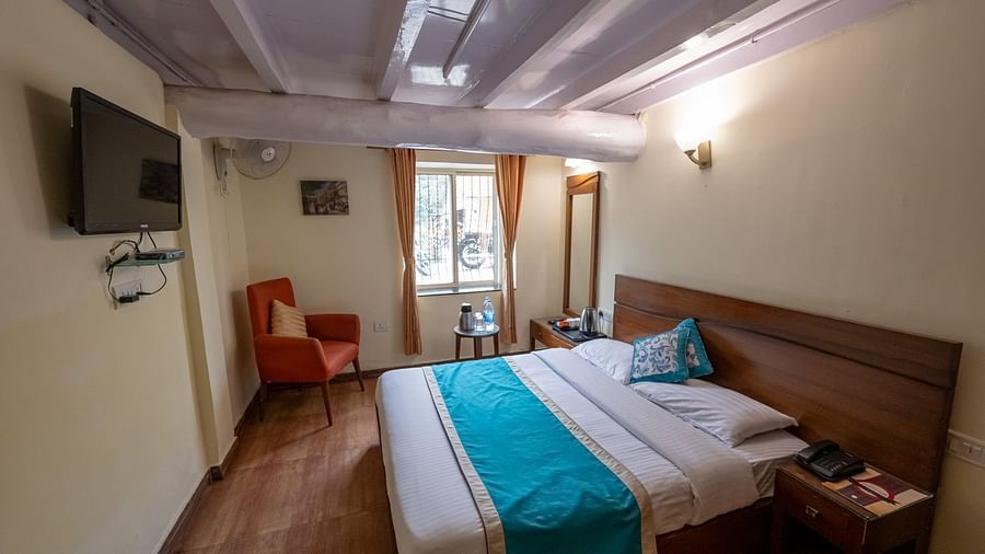 Side view of the standard room with a cosy bed and a TV mounted on the wall at Himalaya Hotel, Nainital
