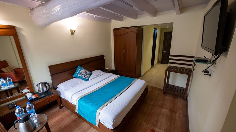 Side view of the standard room with a cosy bed and a TV mounted on the wall at Himalaya Hotel, Nainital