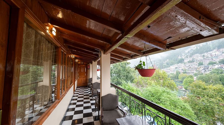 A balcony with a chair offering a lush, green view of the river at Himalaya Hotel, Nainital