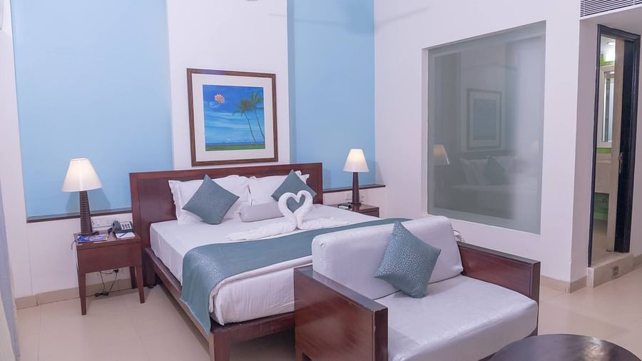 Double bed and couch with white covers but with blue pillows complimenting the room's blue colour at Kyriad Prestige Calangute, Goa