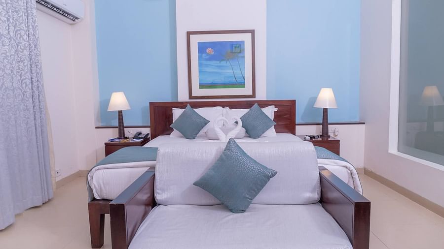 Double bed and couch with white covers but with blue pillows complimenting the room's blue colour at Kyriad Prestige Calangute, Goa