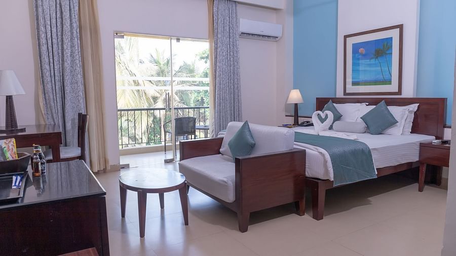 Complete view of the Deluxe room with a double bed, a couch a small tea table and a balcony at Kyriad Prestige Calangute, Goa
