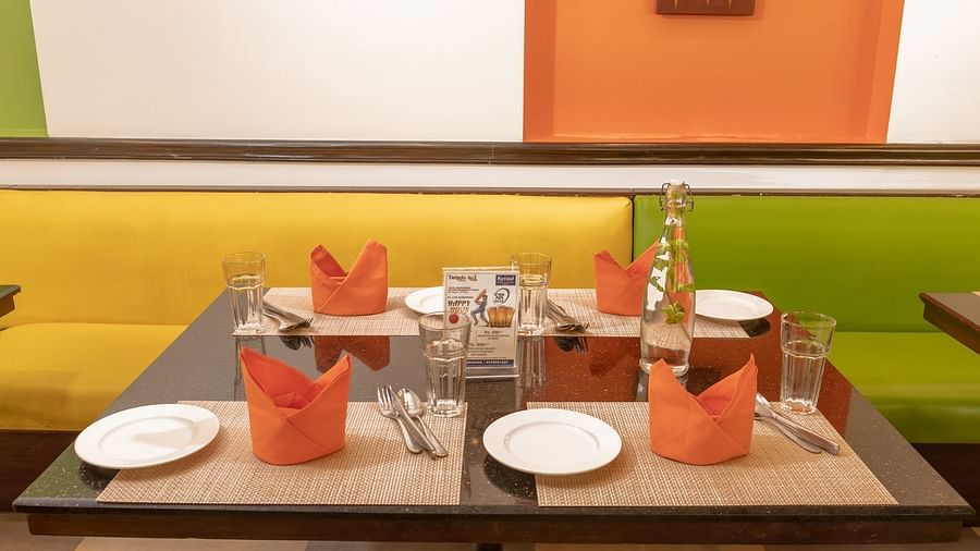 Closer look at the table with orange napkins and white plates at Kyriad Prestige Calangute, Goa