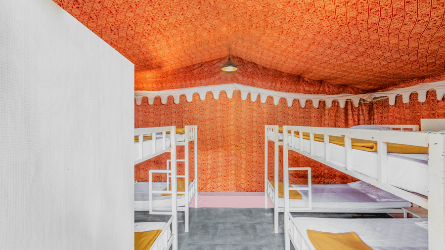PXL 4092-HDRSpacious dormitory interior with white metal bunk beds, vibrant orange patterned ceiling, brick walls, and colourful yellow-red bedding.