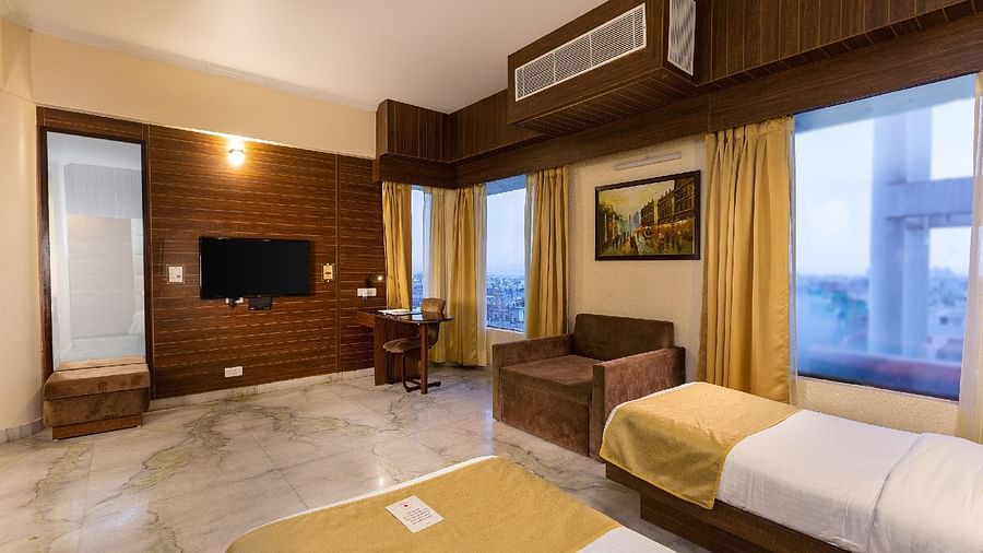 A spacious hotel bedroom with a large bed, an additional single bed, a television, and a window with a view of the outdoors - Pride Premier Dehradun
