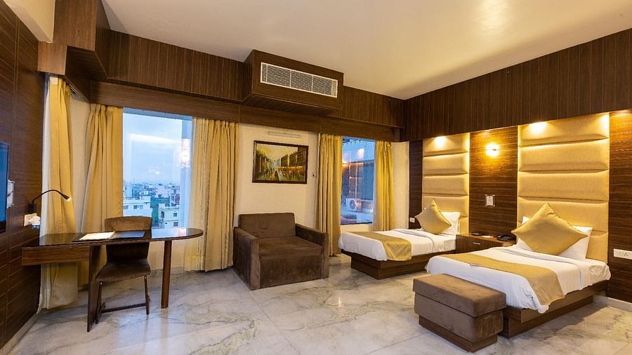  well-appointed hotel room featuring a main bed, an additional single bed, a desk with a chair, and a padded headboard against a dark wood wall - Pride Premier Dehradun