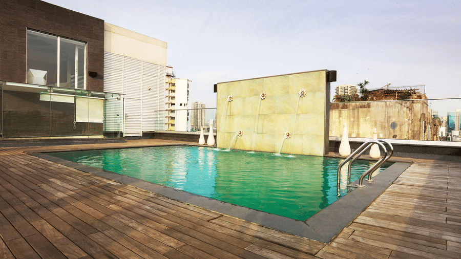 Rooftop pool at The Empresa Hotel with a tiled fountain feature wall, metal entry ladder and glass railing on a wooden deck.