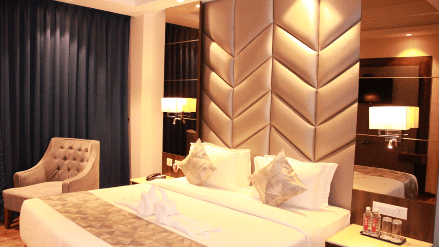 The premier room of Sarovar Portico, Somnath, with a double bed and a lone chair by the window