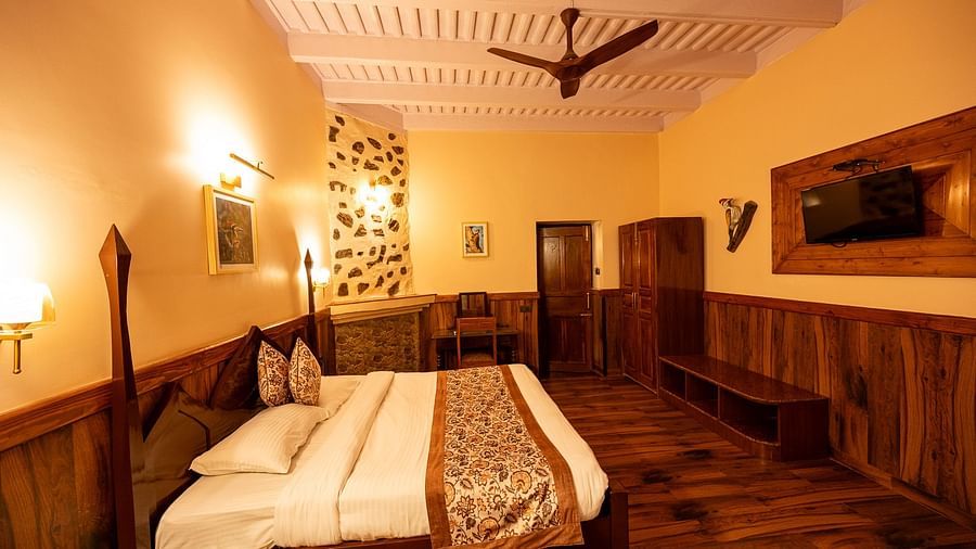 Oak Room at The Pavilion, Nainital features a large bed, wooden paneling, exposed ceiling beams, and warm lighting, creating a traditional feel.