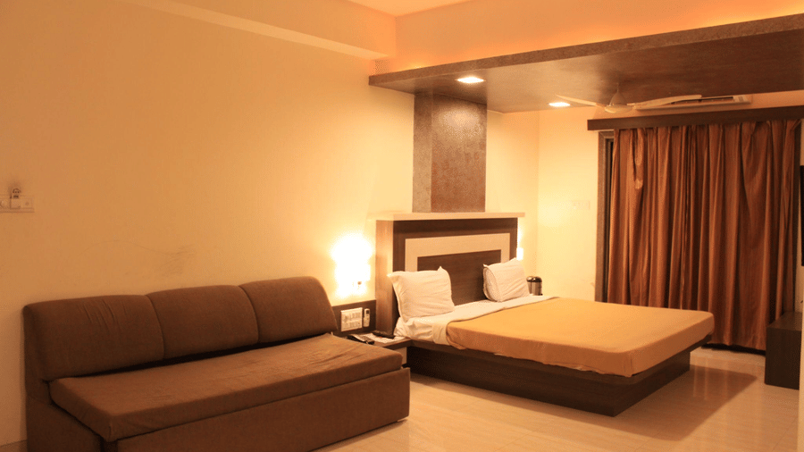 Warmly lit deluxe room featuring a brown fabric sofa couch next to a queen bed with gold-colored linens.