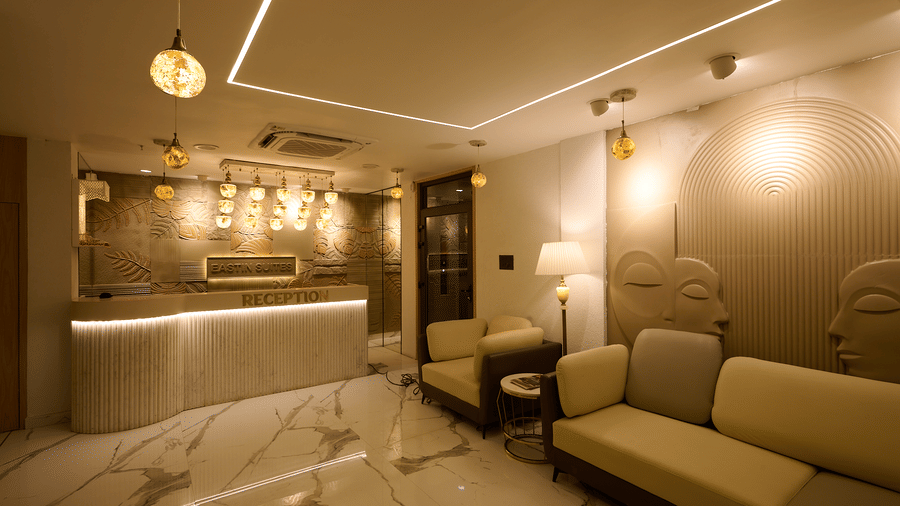 A hotel reception area with a counter, a sofa seating area, marble flooring, and striking lighting fixtures | Voyage Eastin Suites