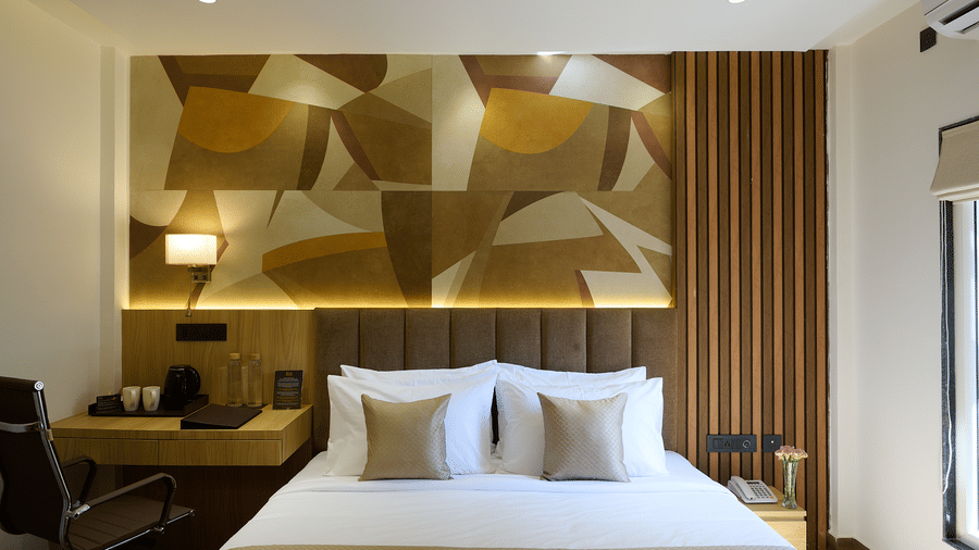 A brightly lit hotel room with a double bed, a geometric patterned accent wall behind the headboard, and a small desk area | Voyage Eastin Suites